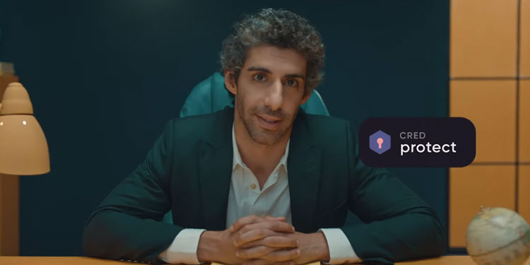 A man in a dark suit sits at a desk with hands clasped, backed by a teal chair and modern office decor; a “CRED protect” badge appears on the right.