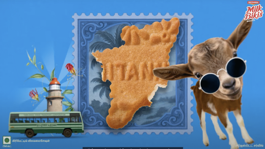 A biscuit bitten into the shape of Tamil Nadu sits against a blue postage stamp backdrop, with ‘TAMIL’ embossed, a playful goat wearing sunglasses, and regional icons like a lighthouse and a green bus.