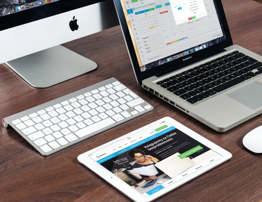 Overhead view of professional workspace with Apple iMac, MacBook Pro, iPad, wireless keyboard and mouse on wooden desk showing calendar and productivity applications