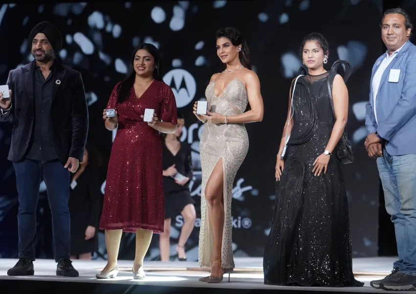 A group of elegantly dressed individuals on stage holding Motorola devices during a product launch event, with a glamorous backdrop featuring Motorola and Swarovski branding.