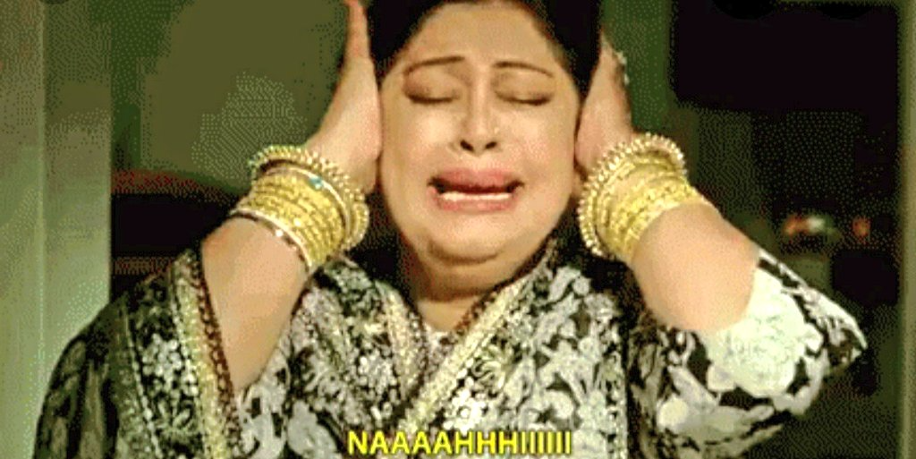 A distressed woman in traditional South Asian attire, hands pressed to her ears, eyes closed and mouth open in a cry, with the caption ‘NAAA AHHHIII’ at the bottom