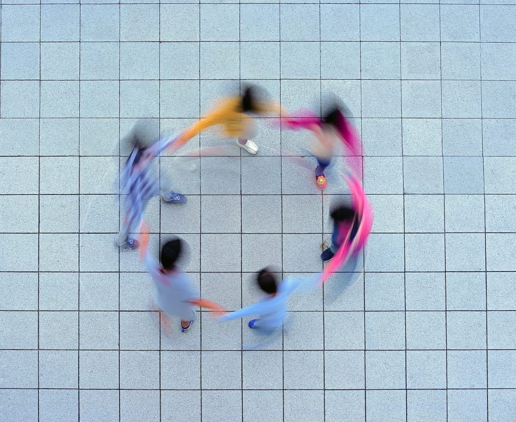 Overhead view of several people standing in a circle on a tiled surface, blurred by movement.
